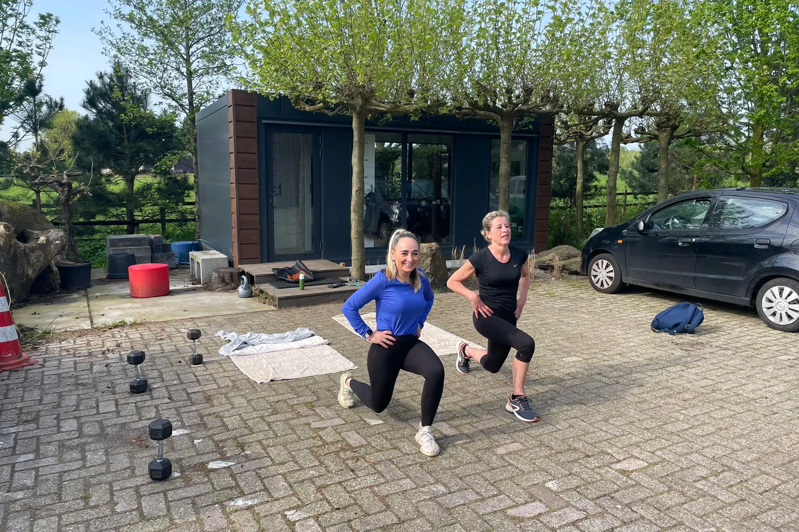 Twee vrouwen doen samen een squat tijdens een personal training buiten