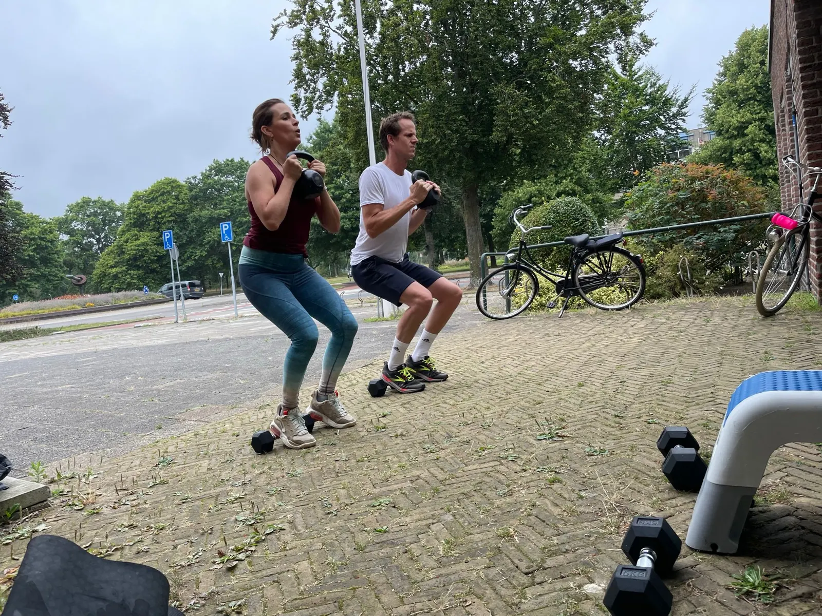 Personal trainer begeleidt een klant tijdens een squat met dumbbells
